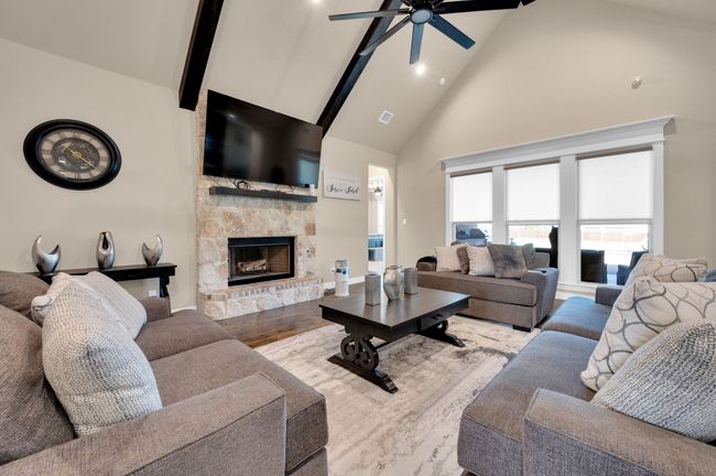 Living area featuring beam ceiling, high vaulted ceiling, wood finished floors, ceiling fan, and a stone fireplace | Image 7