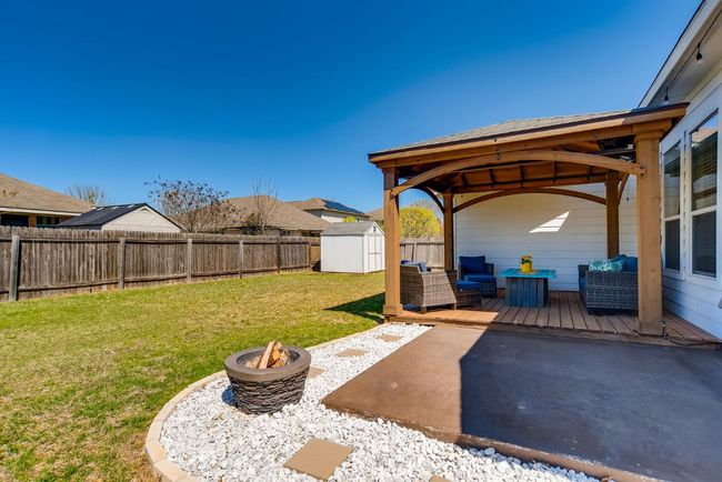 Fenced backyard with a gazebo, a storage unit, a wooden deck, a patio area, and an outdoor living space with a fire pit | Image 25