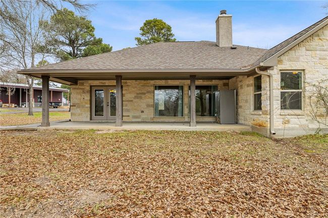 Back of property with stone siding, roof with shingles, and a chimney | Image 21