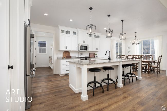Kitchen with light stone counters, hanging light fixtures, appliances with stainless steel finishes, an island with sink, and white cabinets | Image 10