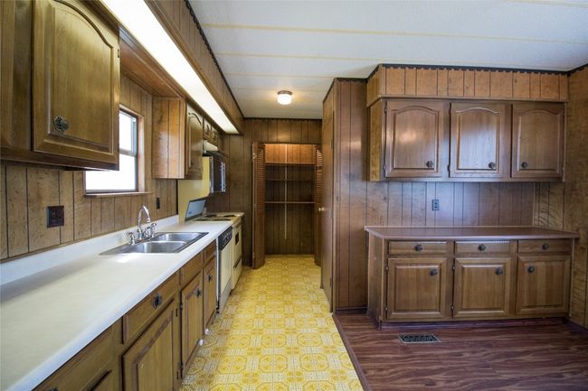 Kitchen with wood walls, stainless steel dishwasher, stove, light floors, and light countertops | Image 7