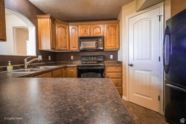 Kitchen featuring black appliances, dark countertops, dark tile patterned flooring, arched walkways, and brown cabinetry | Image 24