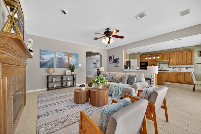 This inviting living space features an open-concept design with a cozy fireplace, modern ceiling fan, and elegant decor. The area seamlessly flows into a spacious kitchen with warm wooden cabinetry and a dining area, creating an ideal setting for entertaining and family gatherings. | Image 5