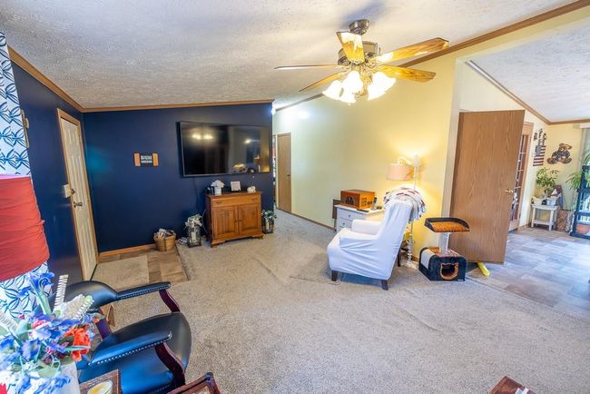 Living area featuring a textured ceiling, ceiling fan, crown molding, and carpet flooring | Image 18