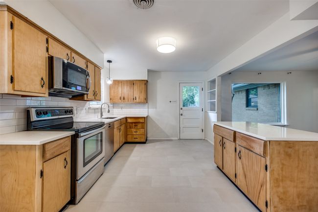 Kitchen featuring appliances with stainless steel finishes, decorative backsplash, light countertops, light flooring, and hanging light fixtures | Image 5