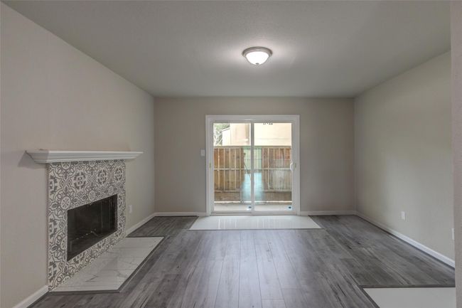 Bright living room with a stylish patterned-tile fireplace and sleek hardwood floors. Features large sliding glass doors leading to a fenced outdoor area, providing ample natural light. | Image 12