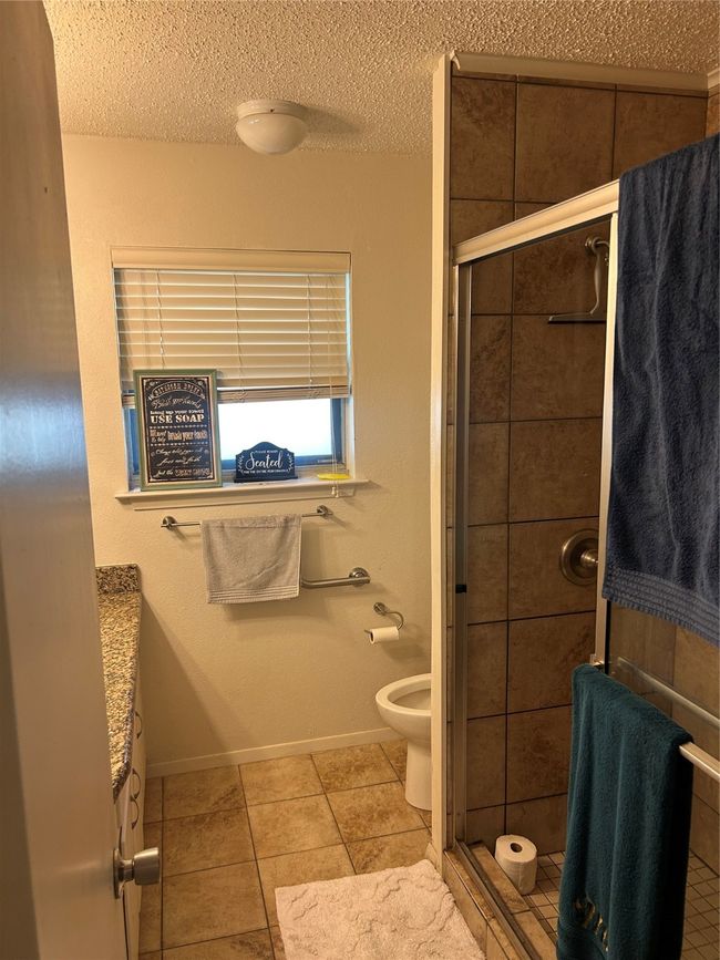 Full bathroom featuring a stall shower, a textured ceiling, tile patterned floors, toilet, and baseboards | Image 14