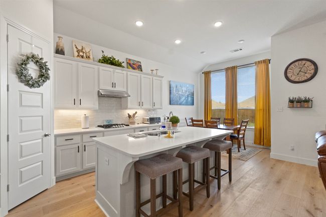 Kitchen with under cabinet range hood, a center island with sink, light wood finished floors, tasteful backsplash, and stainless steel gas cooktop | Image 23