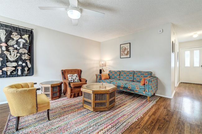 Living area with a textured ceiling, wood finished floors, a ceiling fan, and baseboards | Image 12