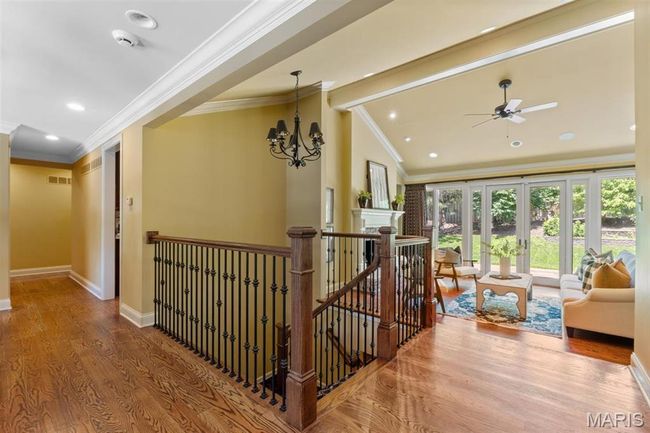 Hall with crown molding, wood finished floors, an upstairs landing, lofted ceiling, and a chandelier | Image 13