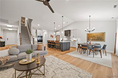 Living room with ceiling fan with notable chandelier, light wood-type flooring, vaulted ceiling, and a fireplace | Image 3