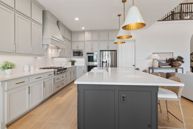 Kitchen featuring gray cabinets, a kitchen breakfast bar, hanging light fixtures, a center island with sink, and light stone countertops | Image 12