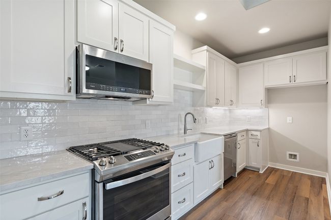 Kitchen featuring stainless steel appliances, a sink, open shelves, light stone counters, and white cabinets | Image 32
