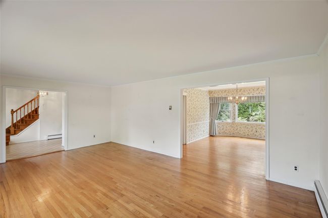 Unfurnished living room featuring a chandelier, light wood-type flooring, stairs, and a baseboard heating unit | Image 13