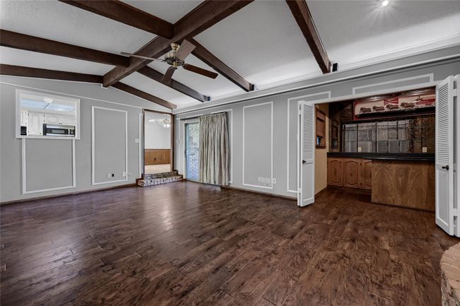 Unfurnished living room featuring a decorative wall, dark wood-type flooring, lofted ceiling with beams, and ceiling fan | Image 12