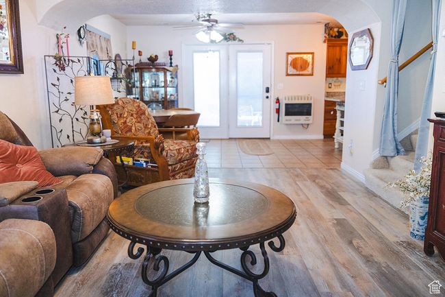 Living area with heating unit, arched walkways, a ceiling fan, light wood-style flooring, and stairway | Image 9