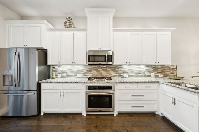Kitchen with stainless steel appliances, white cabinetry, tasteful backsplash, and light stone countertops | Image 5