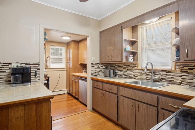 Kitchen with light wood-type flooring, ornamental molding, dishwasher, light countertops, and a sink | Image 8