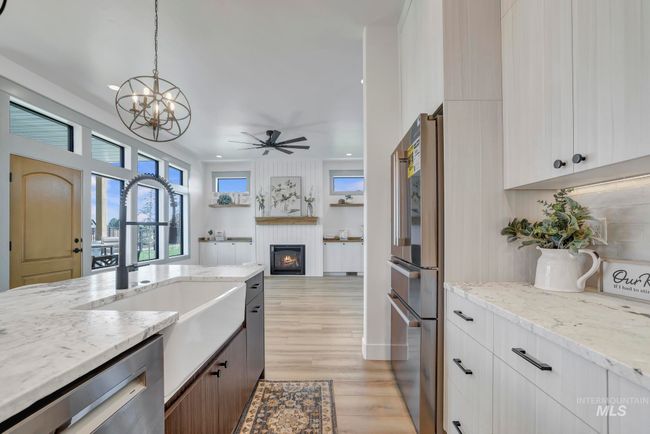 Kitchen featuring stainless steel appliances, a fireplace, a chandelier, a ceiling fan, and light wood-style floors | Image 12