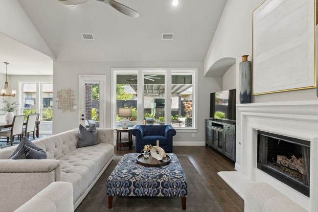 Living room with ceiling fan, dark wood-style flooring, a fireplace with raised hearth, high vaulted ceiling, and a chandelier | Image 8