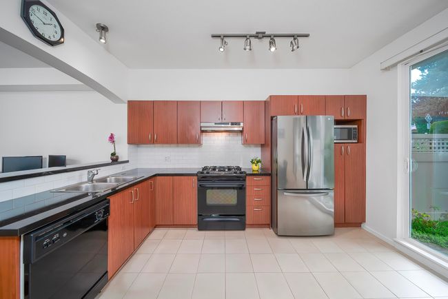 Kitchen with dark countertops, black appliances, under cabinet range hood, decorative backsplash, and a sink | Image 9