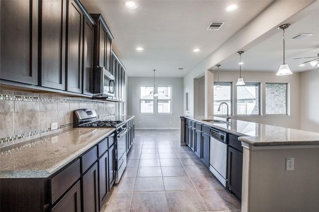 Another view of the Modern kitchen with dark cabinets, stainless steel appliances, granite countertops, pendant lights, and tiled floor. | Image 10