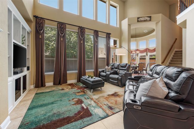 Living area with a high ceiling, light tile patterned flooring, healthy amount of natural light, stairway, and a chandelier | Image 10