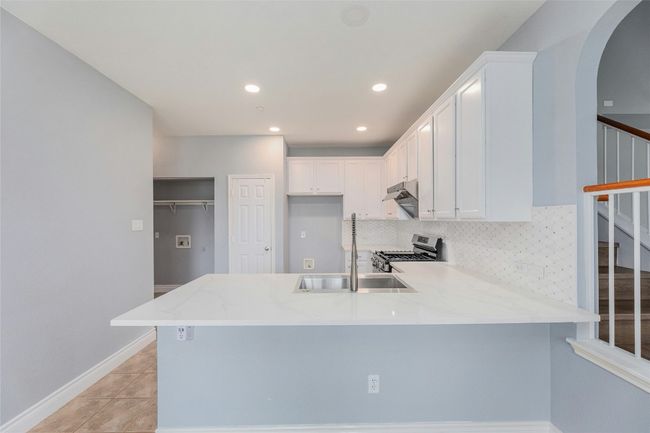 Kitchen featuring stainless steel gas stove, a peninsula, arched walkways, white cabinetry, and under cabinet range hood | Image 11