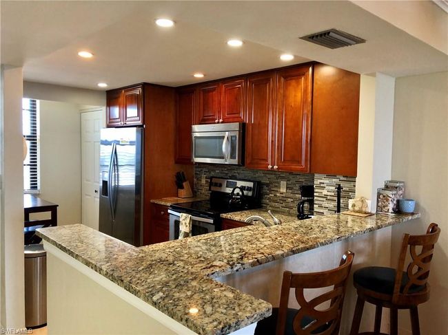 Kitchen featuring a peninsula, light stone counters, visible vents, and appliances with stainless steel finishes | Image 5