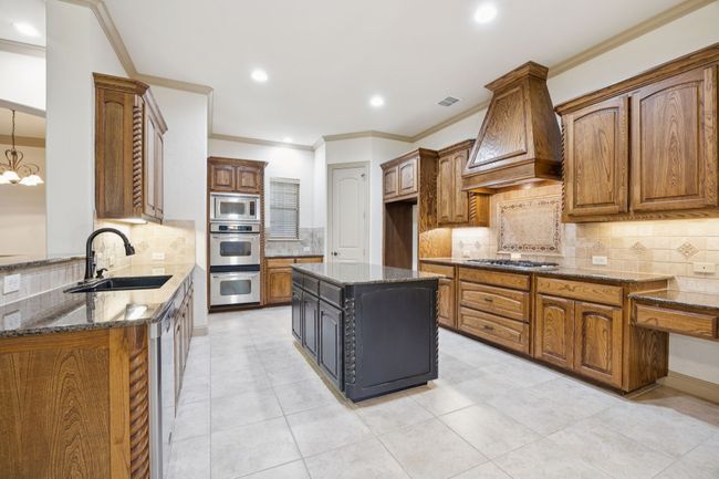 Kitchen with a sink, stainless steel appliances, custom exhaust hood, dark stone countertops, and tasteful backsplash | Image 17