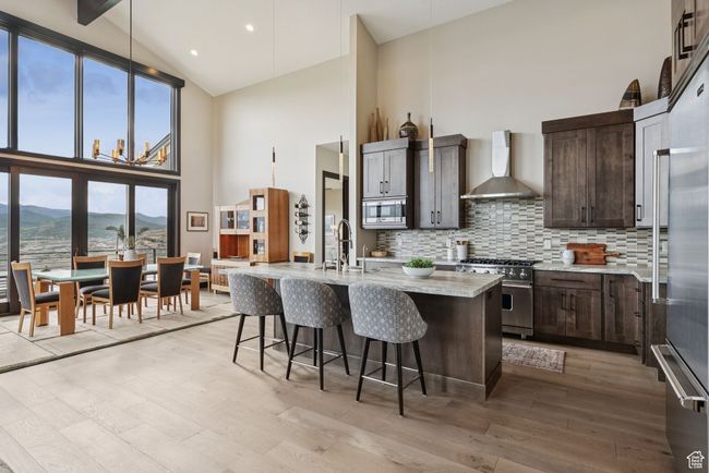 Kitchen with wall chimney range hood, appliances with stainless steel finishes, high vaulted ceiling, backsplash, and light wood finished floors | Image 19