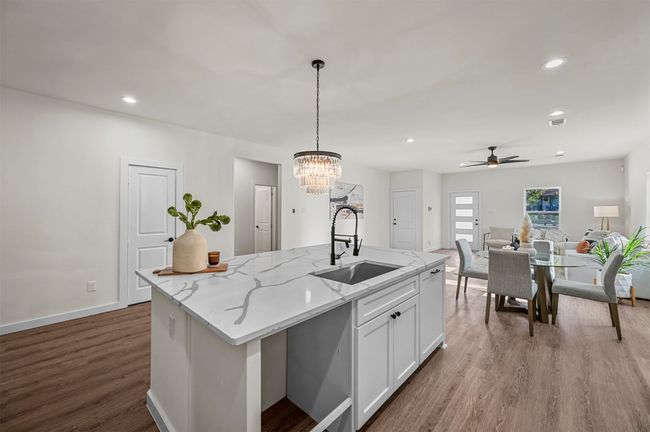 Kitchen featuring wood finished floors, decorative light fixtures, white cabinets, ceiling fan with notable chandelier, and a sink | Image 10