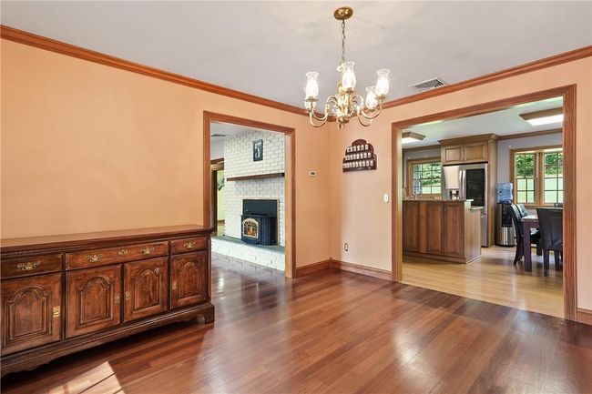 Unfurnished dining area with an inviting chandelier, a brick fireplace, brick wall, hardwood / wood-style floors, and ornamental molding | Image 8
