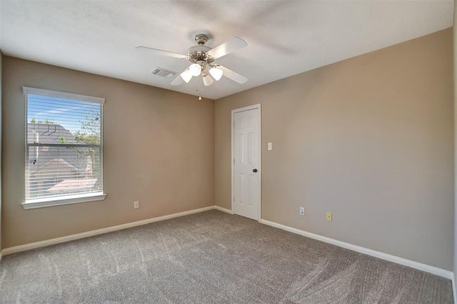 This is a bright, carpeted room with neutral walls and a ceiling fan. It features a window with blinds that lets in natural light and a small closet with a white door. | Image 37