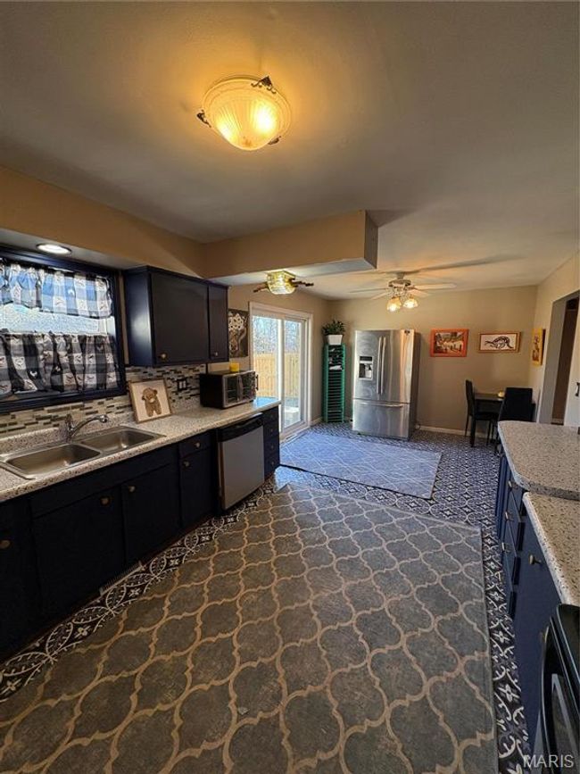 Kitchen with a ceiling fan, dishwashing machine, dark cabinets, fridge, and a sink | Image 12