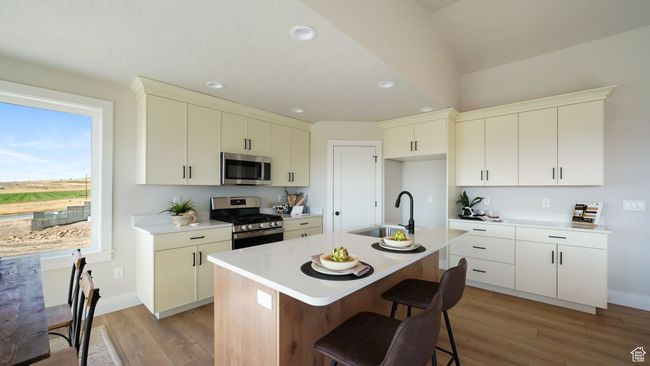 Kitchen featuring appliances with stainless steel finishes, light wood-style flooring, light countertops, a breakfast bar area, and recessed lighting | Image 9