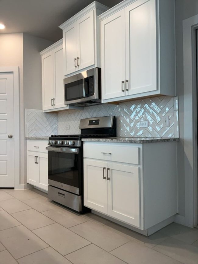 Kitchen with stainless steel appliances, tasteful backsplash, stone countertops, white cabinetry, and light tile patterned flooring | Image 6