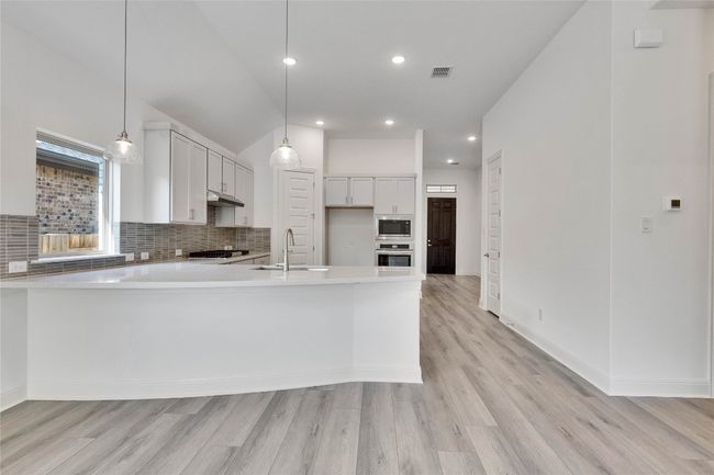 Kitchen featuring a peninsula, tasteful backsplash, light wood finished floors, light countertops, and appliances with stainless steel finishes | Image 6