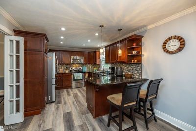 Kitchen featuring appliances with stainless steel finishes, light hardwood / wood-style floors, kitchen peninsula, decorative light fixtures, and ornamental molding | Image 3