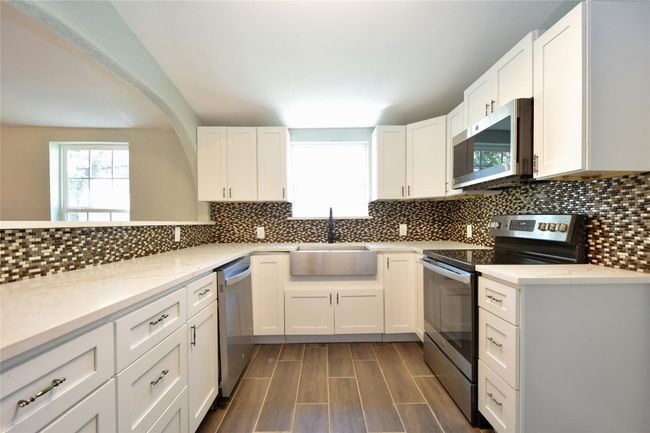 Kitchen featuring appliances with stainless steel finishes, white cabinetry, tasteful backsplash, and light stone counters | Image 14