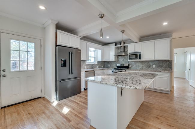 Kitchen with appliances with stainless steel finishes, a sink, wall chimney exhaust hood, beam ceiling, and white cabinetry | Image 12