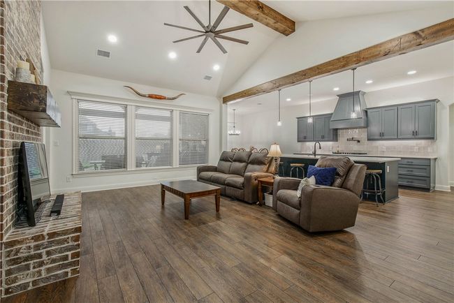 Living room featuring wood-type flooring, a brick fireplace, visible vents, beamed ceiling, and ceiling fan | Image 6