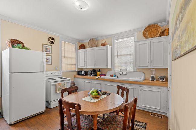 Kitchen featuring white appliances, wood-type flooring, light countertops, white cabinetry, and crown molding | Image 9