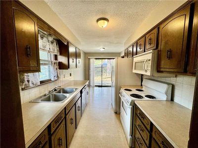 Kitchen with wood cabinets, white appliances, a healthy amount of sunlight, and backsplash | Image 3