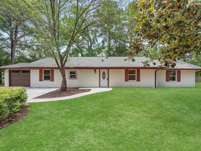 Charming single-story home featuring a clean, white exterior with brick accents, an attached garage, and a lush, landscaped lawn nestled among mature trees. | Image 2