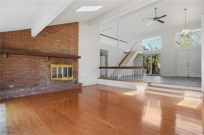 Unfurnished living room with wood finished floors, beamed ceiling, a brick fireplace, high vaulted ceiling, and ceiling fan with notable chandelier | Image 8