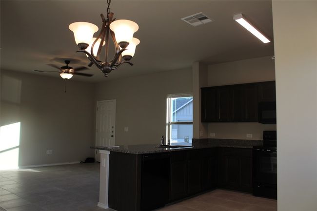Kitchen with black appliances, a sink, ceiling fan, dark stone countertops, and light tile patterned floors | Image 7