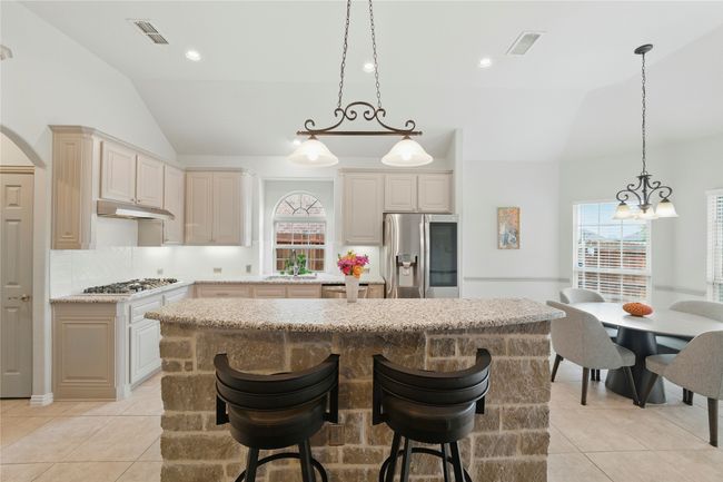 Kitchen featuring lofted ceiling, appliances with stainless steel finishes, a center island, under cabinet range hood, and light tile patterned floors | Image 14