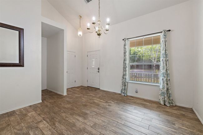Unfurnished room featuring an inviting chandelier, high vaulted ceiling, baseboards, wood finished floors, and visible vents | Image 6