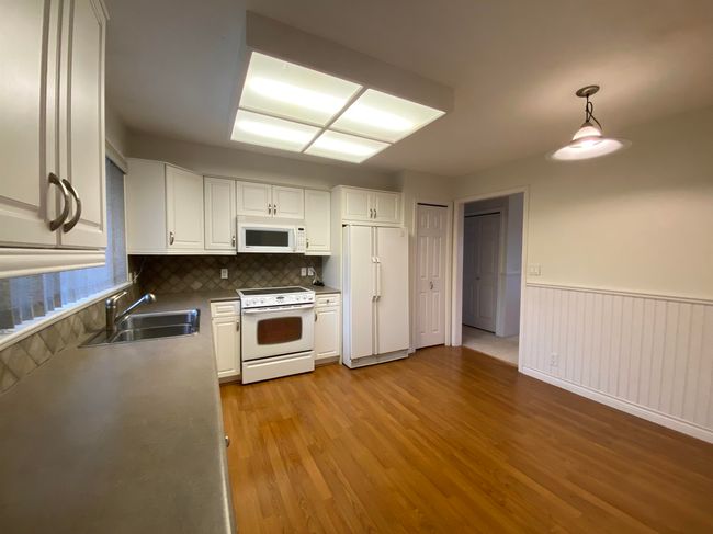 Kitchen featuring white cabinetry, light wood-style flooring, a sink, and white appliances | Image 5
